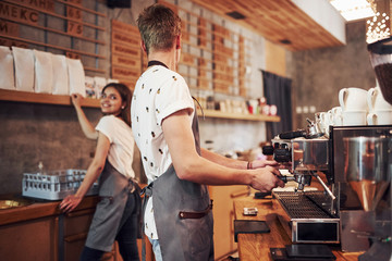 With machine. Two young cafe workers indoors. Conception of business and service