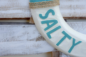 This found typography is carved onto a white and teal wooden life ring or life saver which contains...