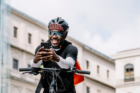 Happy stylish young man with bicycle, smartphone and messenger bag in the city