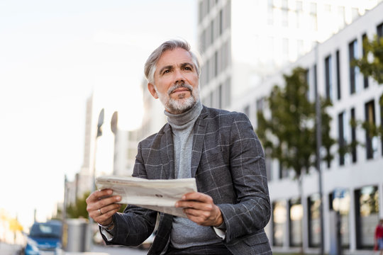 Fashionable mature, businessman reading newspaper in the city
