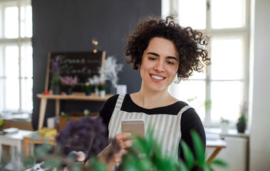 Smiling young woman taking smartphone picture of flowers in a small shop