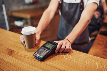 Dring and system for digital paying. Young male cafe worker indoors. Conception of business and service