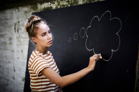 Pensive young woman drawing a thought bubble on a blackboard