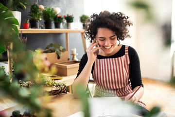 Happy young woman on the phone in a small shop with plants