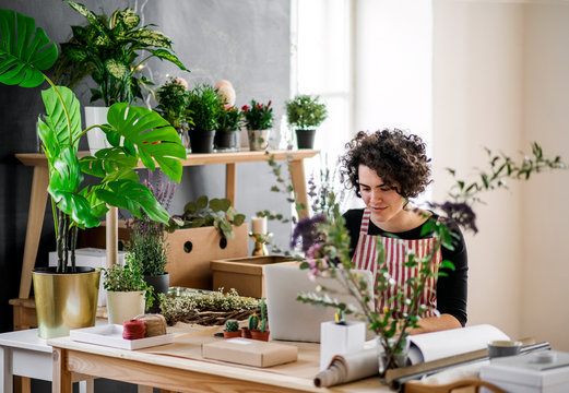 Young woman using laptop in a small shop with plants
