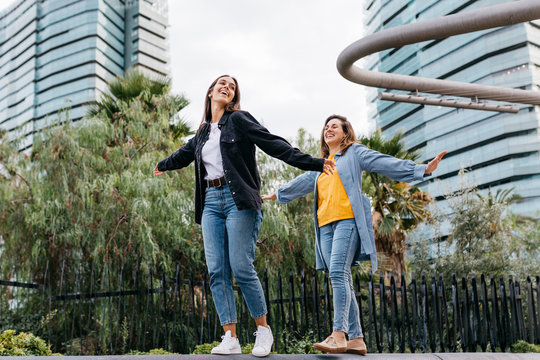 Two friends walking over a bench with open arms and laughing
