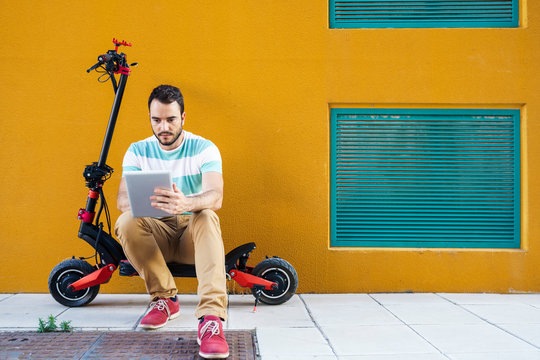 Portrait of man sitting on electric scooter using digital tablet