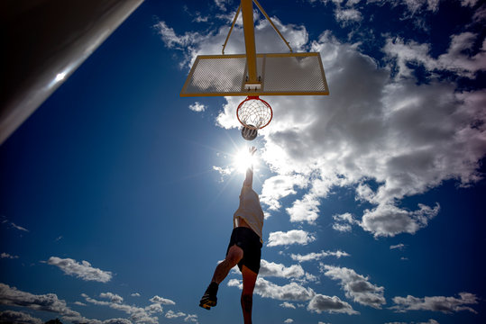 Man playing basketball, dunking against the sun