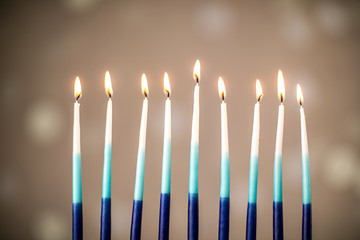 A silver menorah for the Jewish holiday Hanukkah with burning glowing eight candles on fire lit up on a beige background with copy space