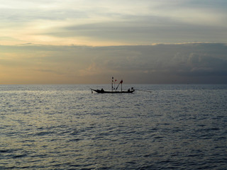 Obraz premium lonely small fishing boats on the open ocean against a background of storm clouds at sunset 