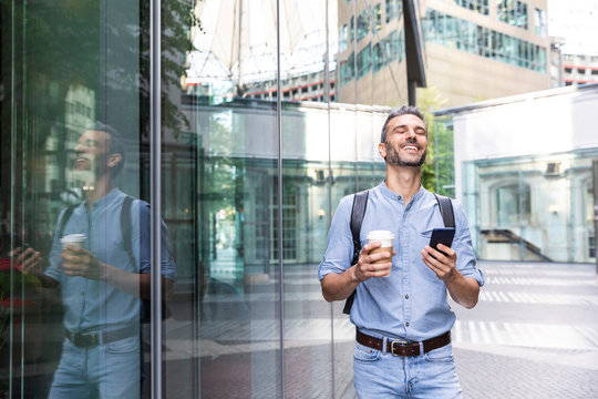 Smiling businessman holding cup of coffee and smartphone in the city, Berlin, Germany