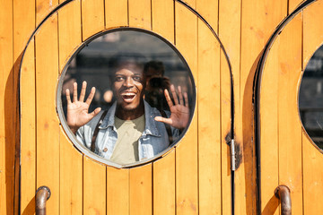 Young man behind wooden door, looking amazed through round window