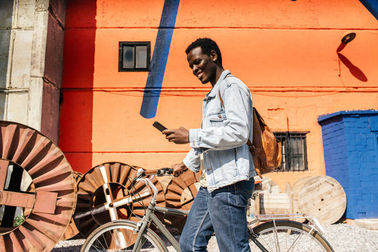 Relaxed young man commuting in the city with hos bicycle, using smartphone