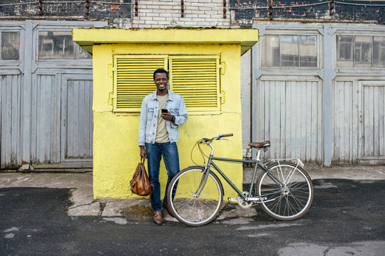 Young man with smartphone, waiting in front of yellow junction box