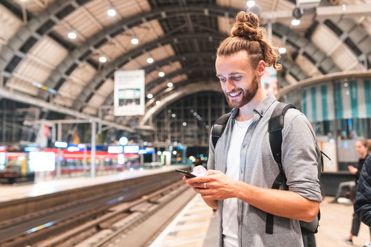 Young smiling man using smartphone on train station