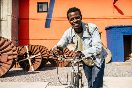 Relaxed young man commuting in the city with hos bicycle, using smartphone
