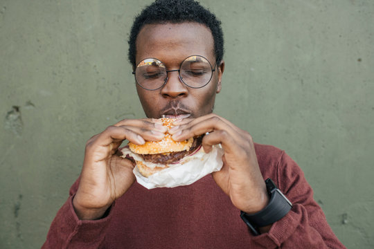 Young man eating cheeseburger, with eyes closed