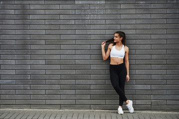 Young sportive brunette with slim body shape against brick wall in the city at daytime