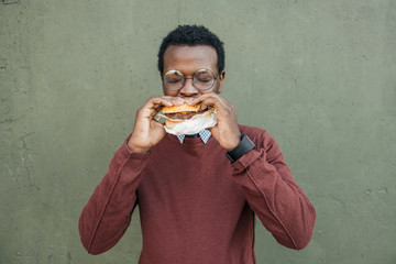 Young man eating cheeseburger, with eyes closed