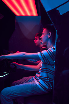 Teenage friends playing with a driving simulator in an amusement arcade