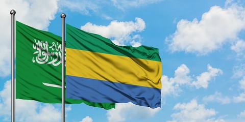 Saudi Arabia and Gabon flag waving in the wind against white cloudy blue sky together. Diplomacy...