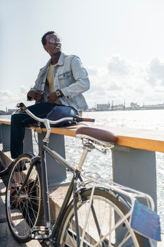 Young man with bicycle sitting on railing by the sea
