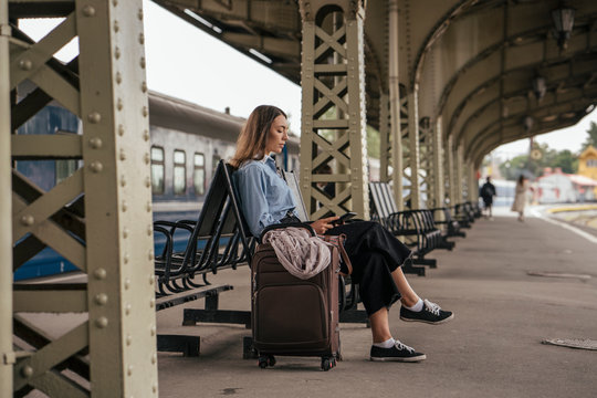 Young female, traveler waiting on train station, using e-book