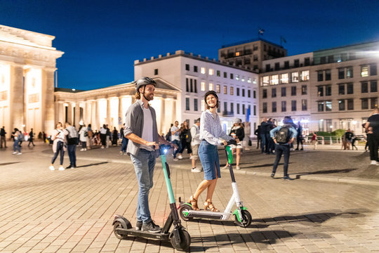 Young couple with electric scooters at Brandenburg Gate at night, Berlin, Germany