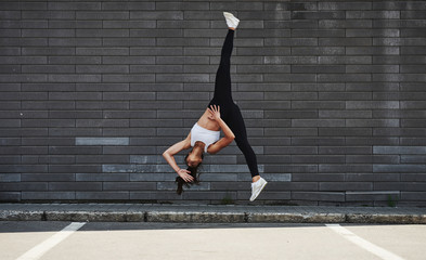 Doing crazy parkour and athletic stunts. Young sportive brunette with slim body shape against brick...