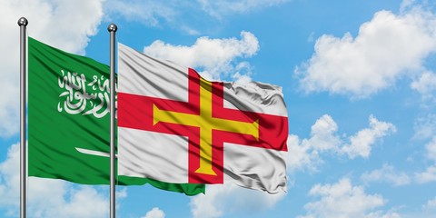 Saudi Arabia and Guernsey flag waving in the wind against white cloudy blue sky together. Diplomacy concept, international relations.