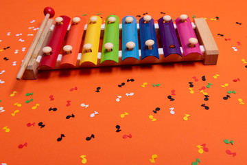 Wooden xylophone in rainbow colors for children an isolated on orange. Paper colorful musical notes...