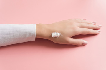 Fototapeta premium Hand of beautiful young girl with cream on pink pastel background. Concept template feminine blog, social media, beauty concept