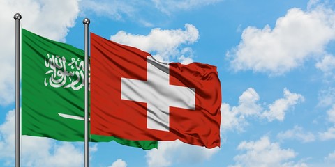 Saudi Arabia and Switzerland flag waving in the wind against white cloudy blue sky together. Diplomacy concept, international relations.