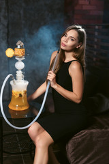Portrait of young beautiful girl smoking hookah in lounge. The pleasure of smoking. Shisha bar party concept