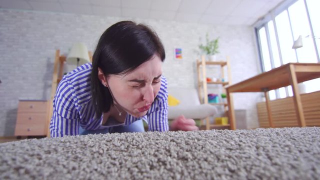 young woman in the living room is sniffing a carpet that smells bad