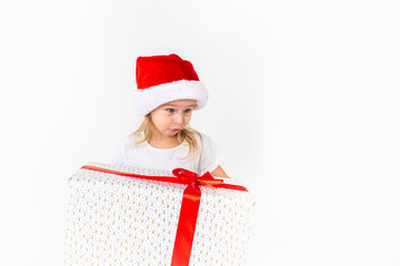 Little smiling girl in santa helper hat holding white gift with red ribbon on white isolated background. Christmas, winter, happiness concept.