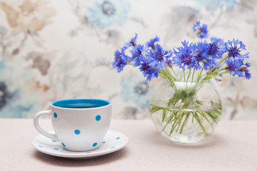 Tea in cup with dots and vase of cornflower flowers - card with still life