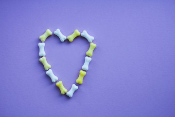 Naklejka na ściany i meble symbolic image of a heart on a purple background with candy in the form of bones.