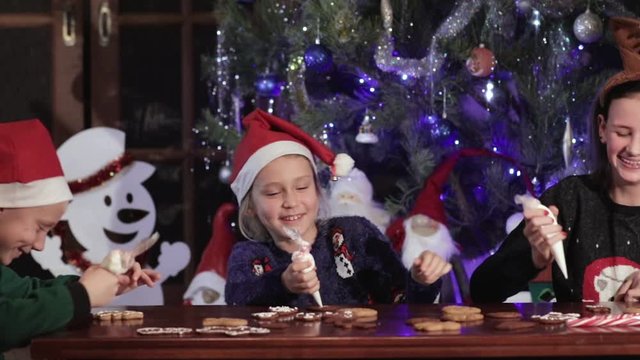 Children paint Christmas gingerbread cookies. They joke and laugh merrily