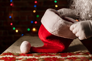 Christmas Santa claus putting his hat on the table with a background of colored lights on a brick wall. Christmas Concept