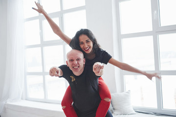 Hands to the different sides. Playful couple in black and red clothes having fun in the white room in daytime