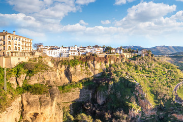 Obraz premium Ronda, Spain: Landscape of white houses on the green edges of steep cliffs with mountains in the background.