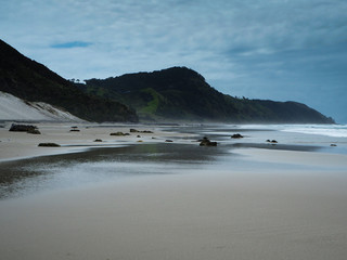 sandy beach with black rocks on the background of green mountain slopes