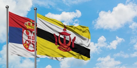 Serbia and Brunei flag waving in the wind against white cloudy blue sky together. Diplomacy concept, international relations.