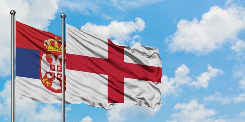 Serbia and England flag waving in the wind against white cloudy blue sky together. Diplomacy concept, international relations.