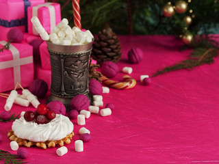 Christmas still life with meringue and waffle. A cup of hot drink with marshmallows on a background of fuchsia color. Festive Christmas tree, decorations and gifts. Close-up. Copy space