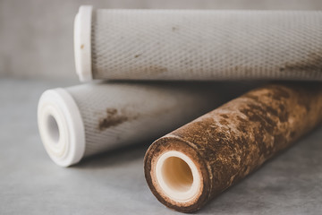 Old used cartridges for a water filter on a gray background.