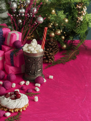 Christmas still life with meringue and waffle. A cup of hot drink with marshmallows on a background of fuchsia color. Festive Christmas tree, decorations and gifts. Close-up.