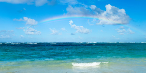 Rainbow and sunrise on the beach of a tropical bay