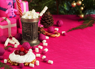 Christmas still life with meringue and waffle. A cup of hot drink with marshmallows on a background of fuchsia color. Festive Christmas tree, decorations and gifts. Close-up. Copy space